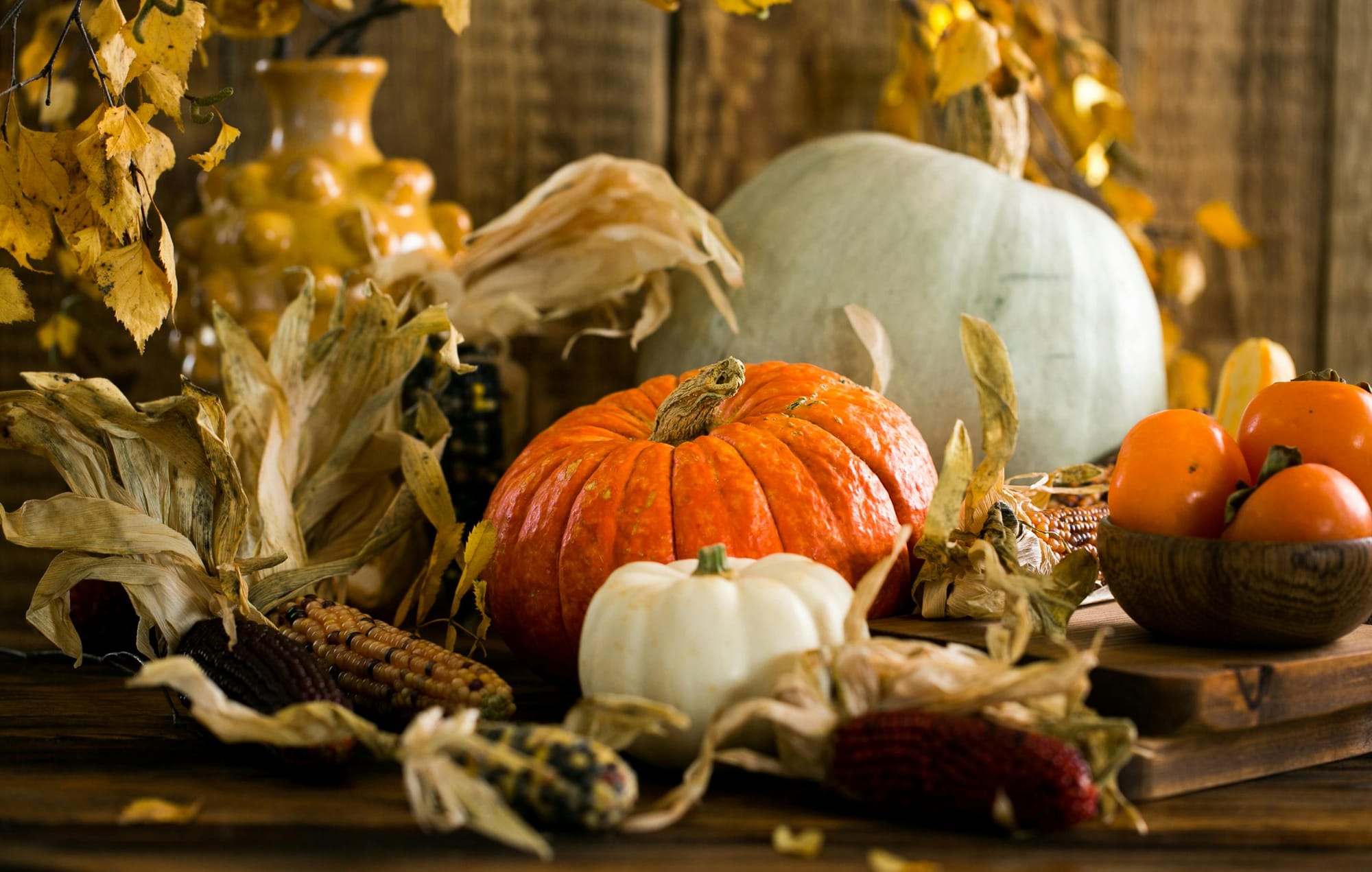 A rustic autumn tablescape with pumpkins, gourds, dried leaves, and decorative corn arranged on a wooden surface.