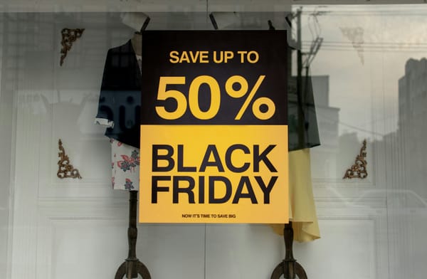 A Black Friday sale sign in a shop window reading “Save up to 50%,” displayed in front of mannequins wearing clothing.